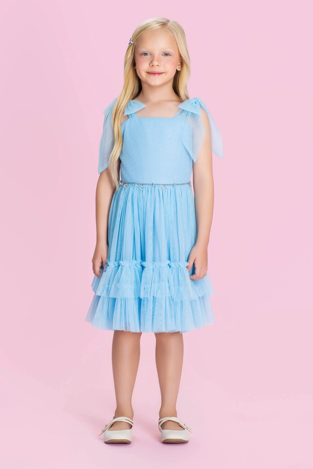 Vestido infantil azul Petit Cherie visto de costas, com laços nos ombros e saia de tule com babados.