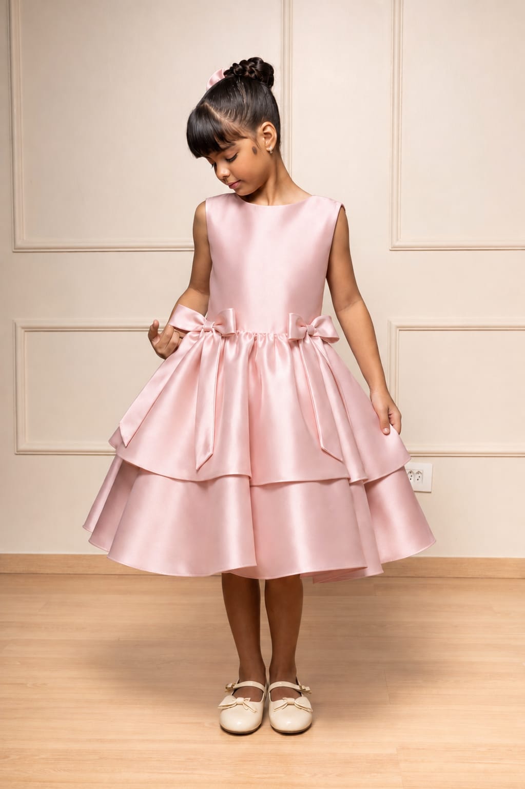 Menina usando vestido infantil de festa Buá em cetim rosê, sem mangas, com dois laços na cintura e saia rodada em duas camadas.