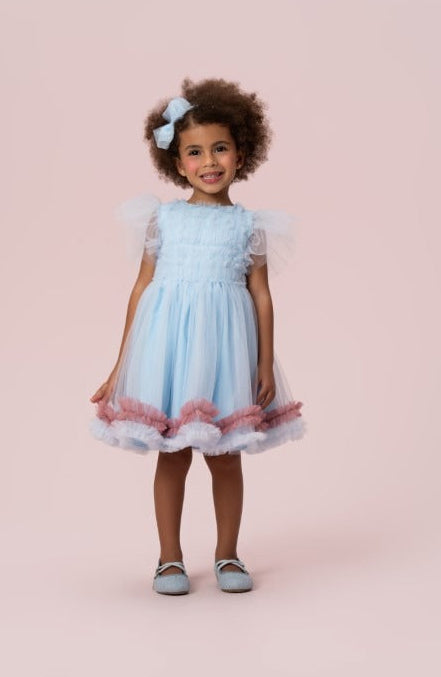 Menina com vestido infantil azul Petit Cherie, mangas em tule e saia com babados rosa e azul na barra.